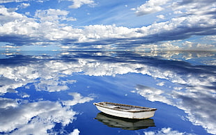 white and brown wooden boat in body of blue water with sky and clouds background