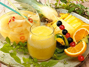 pineapple juice on punch bowl and a pitcher of pineapple juice next to sliced orange