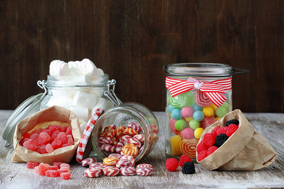 Variety of candies in jars on gray wooden surface HD wallpaper