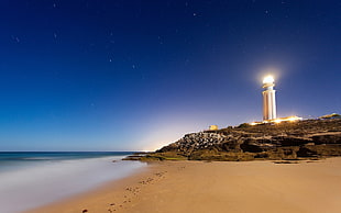 white lighted lighthouse beside body of water HD wallpaper