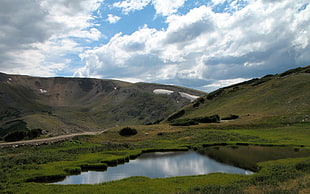 body of water surrounded by green mountain under cloudy blue sky during daytime