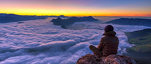 man seating on the peak of the mountain HD wallpaper