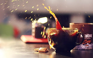 filled translucent brown tea cup beside brown labeled cup on top of brown wood-top table