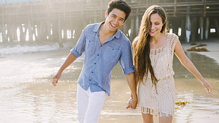 man and woman holding hands near body of water during daytime