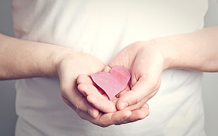 person wearing white shirt holding pink heart paper cut