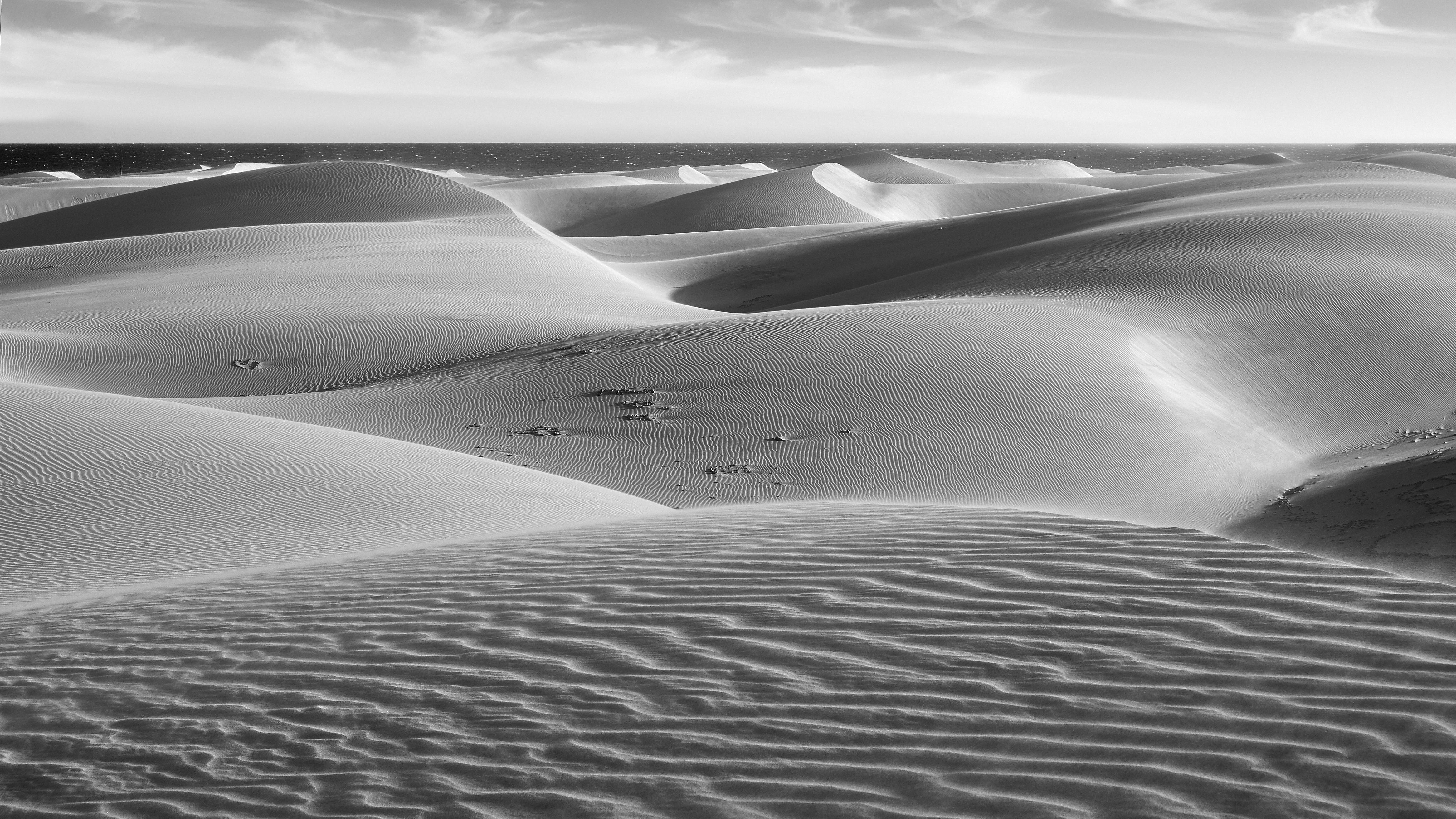 grayscale of sand dune under cloudy sky