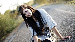 woman in white 3/4 sleeve shirt sitting on black asphalt road during daytime