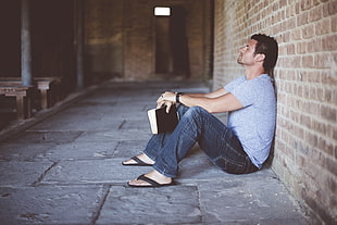 man in gray crew-neck shirt sitting while holding black bible HD wallpaper