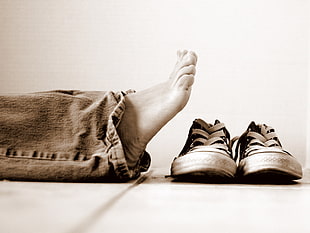 grayscale photo of a person wearing jeans near pair of sneakers