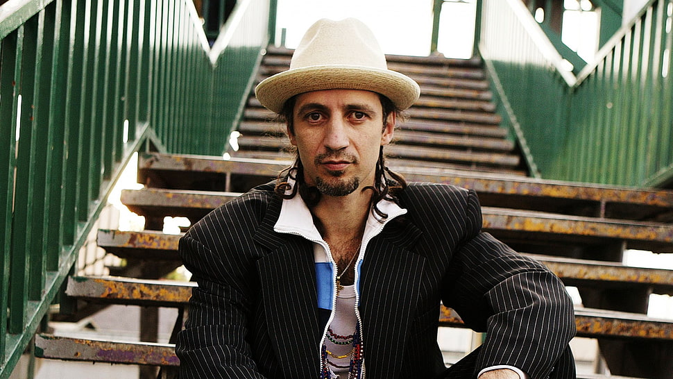 man wearing black and gray pinstripe printed suit jacket sitting on brown steel stairs during daytime HD wallpaper