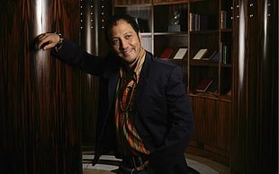 man in black suit jacket standing near brown wooden shelf HD wallpaper