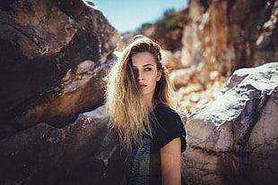 blonde woman wearing black top standing near brown rock HD wallpaper