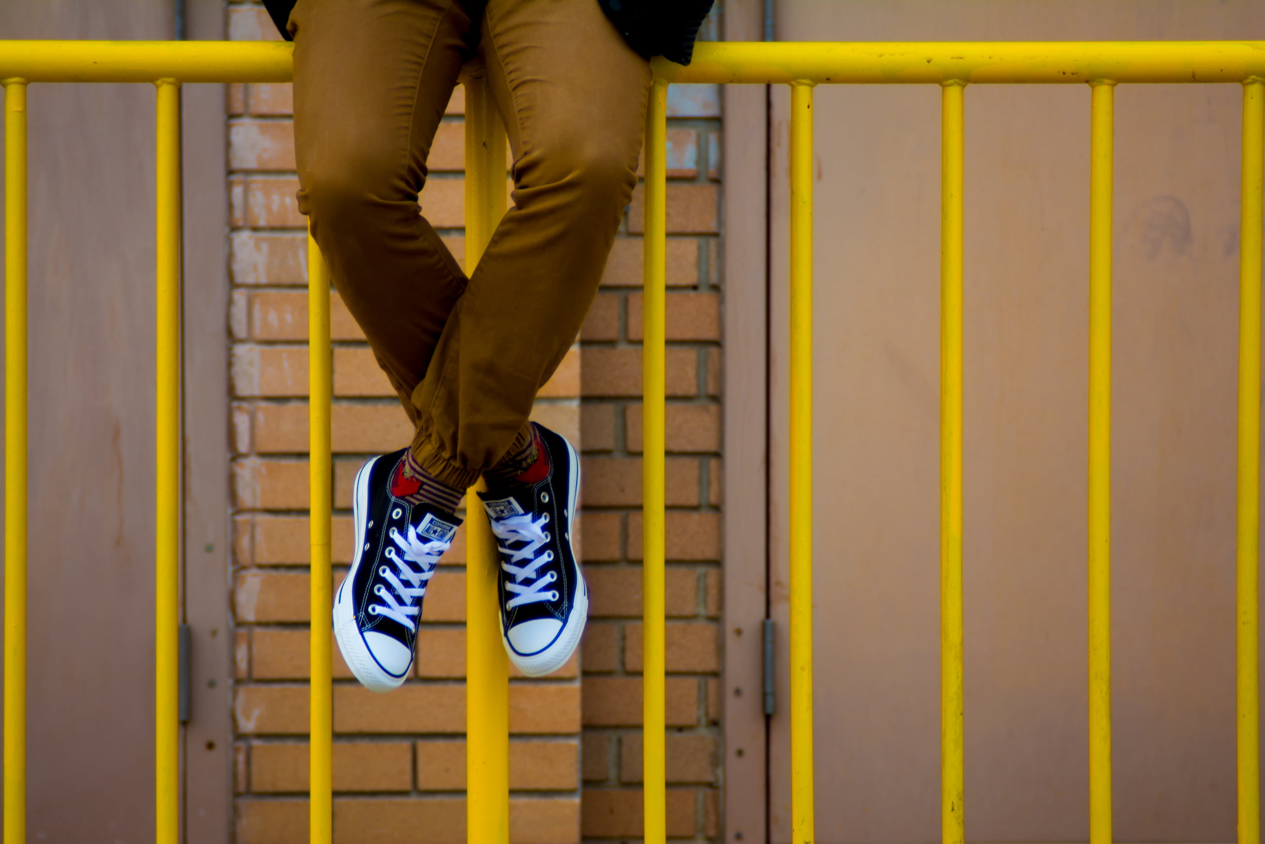 Person with brown pants and black-and-white lace-up low-top sneakers  sitting on yellow metal railings HD wallpaper | Wallpaper Flare