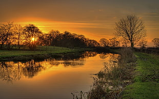 green grass field in between of body of water during sunrise