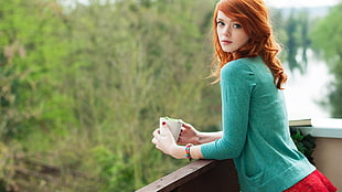 selective focus photography of woman wearing green cardigan leaning on wooden rail while holding white mug HD wallpaper