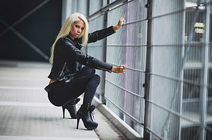 woman wearing black jacket, pants, and and stiletto platform booties sitting near grey metal barrier HD wallpaper