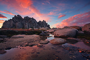 landscape photo of gray stone on body of water in sunset