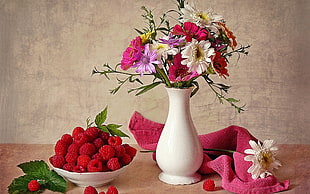 white ceramic vase with flowers beside strawberry fruits