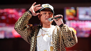 man wearing gold-colored and black coat and white cap holding microphone HD wallpaper