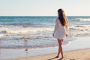 woman wearing white long-sleeved dress standing near seashore on white sand during golden hour HD wallpaper