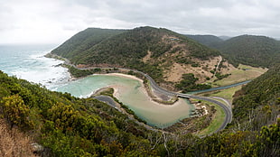 road beside seashore near green mountains