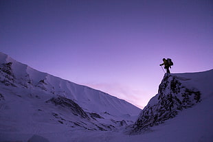 low angle photo of man wearing backpack holding ski poles near snow-caped cliff HD wallpaper