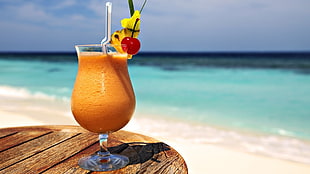 clear footed glass with beverage and straw on brown wooden table