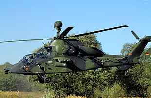 green and black camouflage attack helicopter near tree under blue sky during daytime HD wallpaper