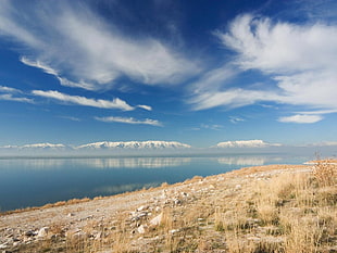 snow covered mountain range in front of blue body of water during daytime