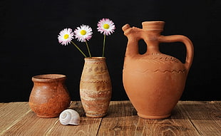 three white Chrysanthemum flowers in brown vase near two vases