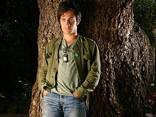 man wearing green jacket standing near tree HD wallpaper