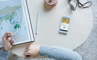 person wearing gray sweater sitting in front table holding world map print beside smartphone HD wallpaper