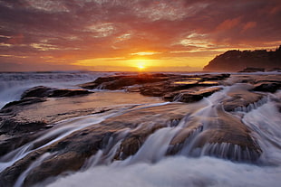 body of water near black rocks at daytime HD wallpaper