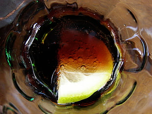 clear glass bottle filled with rum-cola and green lime on brown wooden table top