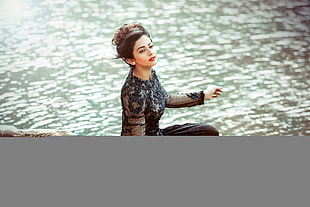 woman with black long-sleeved floral crew-neck dress sitting by the water during daytime