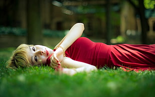 depth of field of woman in red dress lying on green grass HD wallpaper
