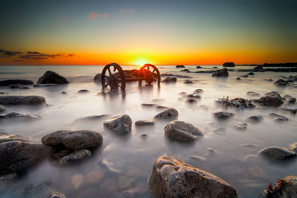 carriage axle with wheels on water with stones during golden hour HD wallpaper