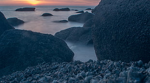 photo of of body of water with concrete stones during sunset