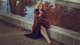 woman sitting on gray concrete surface beside body of water