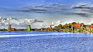 blue body of water near three windmills and village houses under blue and white cloudy sky during daytime HD wallpaper