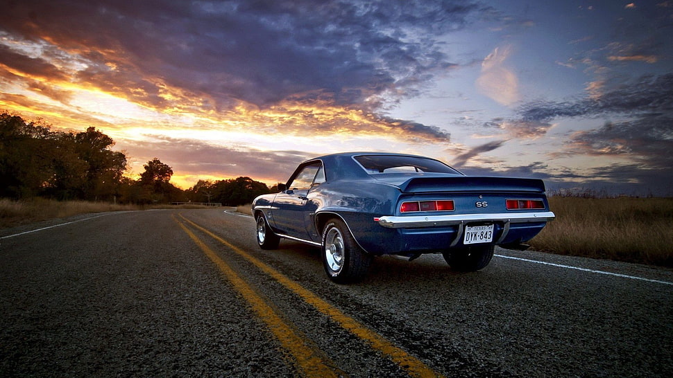 classic blue Ford Mustang on open road during golden hour HD wallpaper