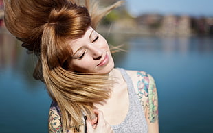 focused photo of woman with blonde hair closing her eyes in gray tank top