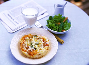 round melted cheese topped food on white ceramic plate beside bowl of green salad and footed glass of milk HD wallpaper