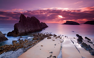 gray concrete rock formation on sea during sunset