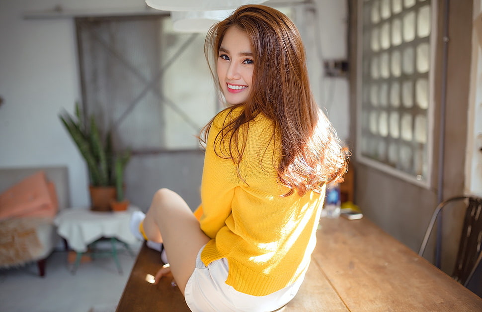 woman wearing yellow long-sleeved top sitting on brown wooden table taking picture HD wallpaper