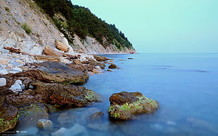 blue sea water beside brown mountain at daytime