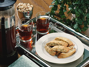 sliced bread on round white ceramic plate near two clear glass mug both on rectangular stainless steel tray