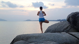 person wearing white tank top and blue shorts while meditating on top of gray stone HD wallpaper
