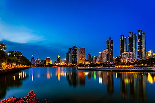 lighted high-rise building near calm water under blue sky wallpaper HD wallpaper