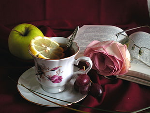 white and pink floral ceramic teacup filled with tea with sliced lemon and teaspoon on white ceramic saucer beside green apple, pink rose flower, eyeglasses and book HD wallpaper